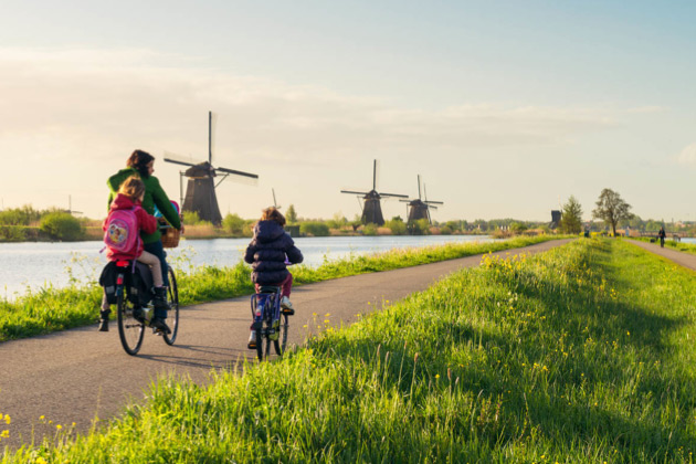 Moeder fietst met kinderen langs rij molens op een ringdijk